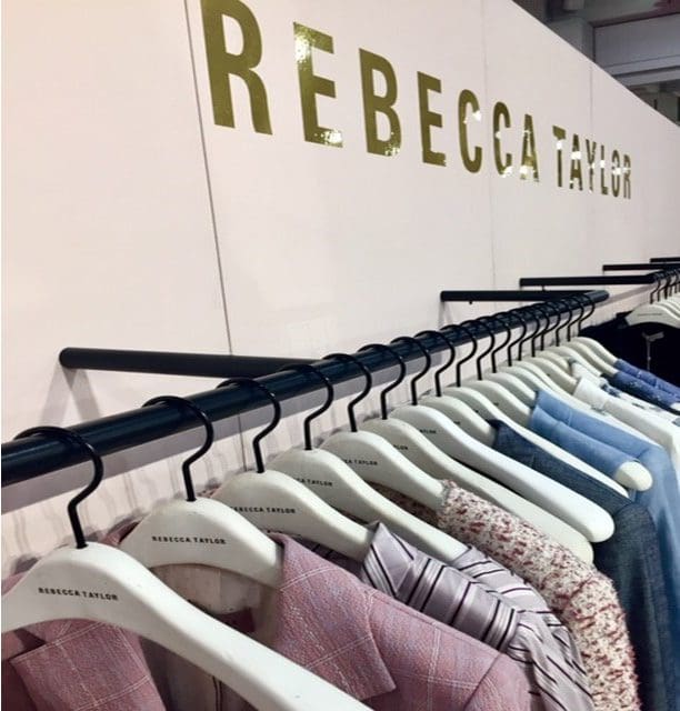 Clothes hang from a rack labeled "Rebecca Taylor," showcasing a variety of stylish garments in pastel tones. Perfect for fashion retail context.