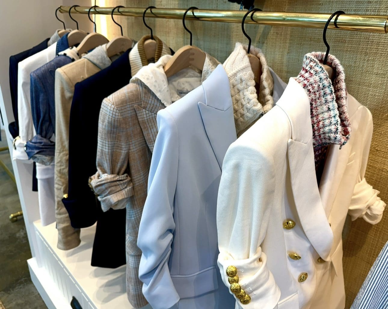 Stylish blazers in varied colors hang on gold rack in boutique.