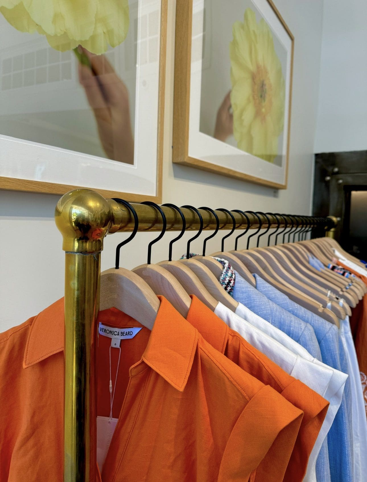 Colorful garments hang beneath floral artwork in boutique.