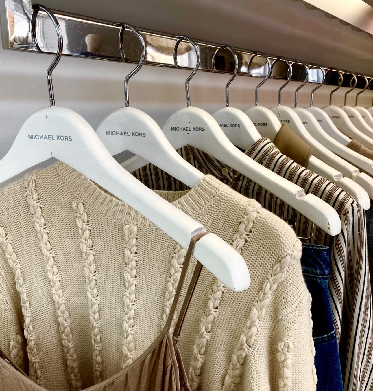 Michael Kors clothes hang on white hangers: sweater, dress.