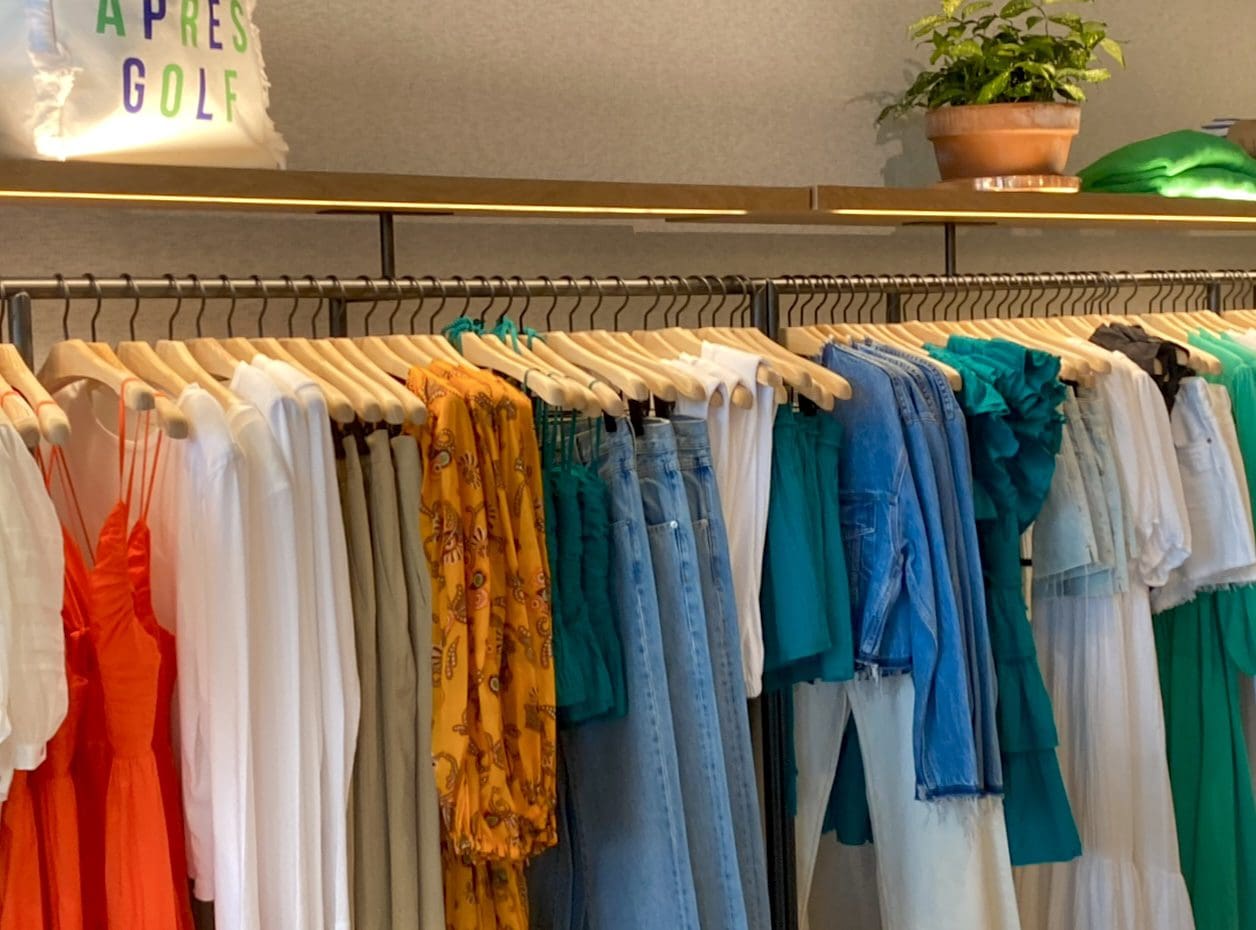 Colorful dresses, tops, jeans hang amid greenery.