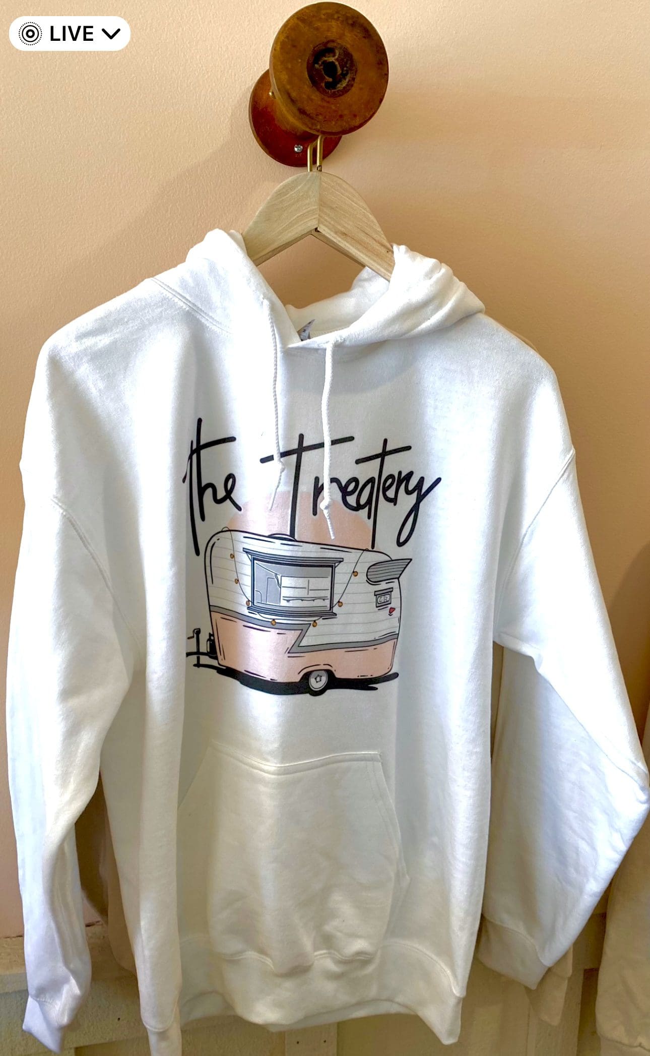 White hoodie with vintage trailer graphic reading "The Treatery."