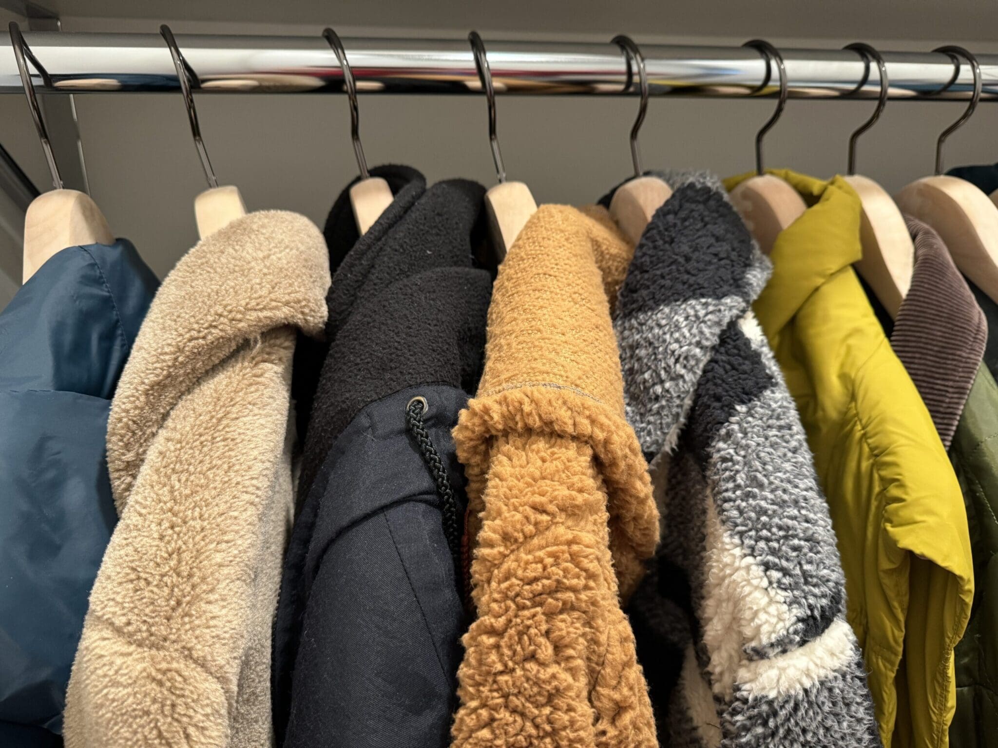 Varied winter jackets in many textures hang on rack.