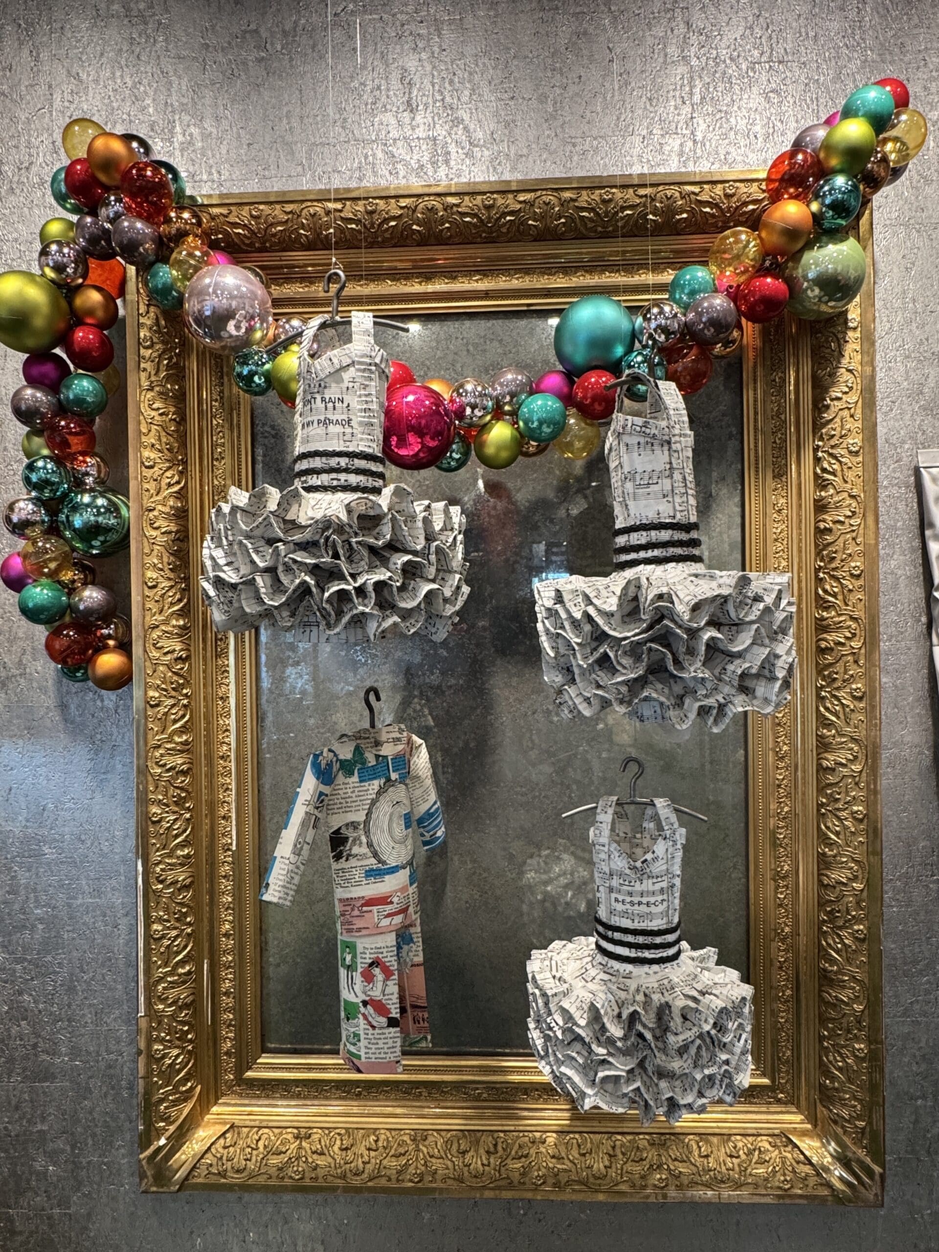 Three newspaper dress forms, paper outfit, gold frame, ornaments.