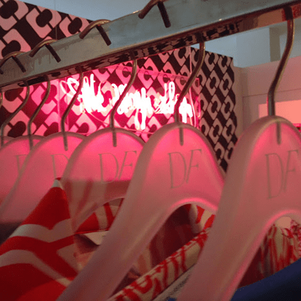 Colorful clothes on clear hangers, pink-lit background.