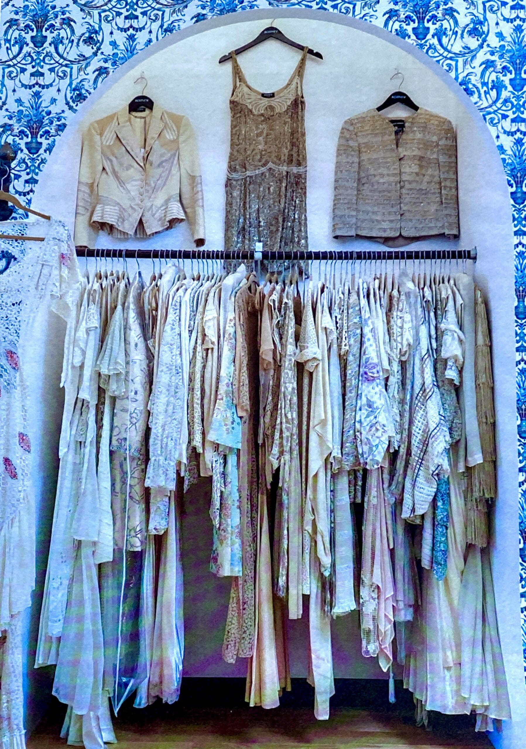Neutral-toned women's clothing displayed against blue-patterned wall.