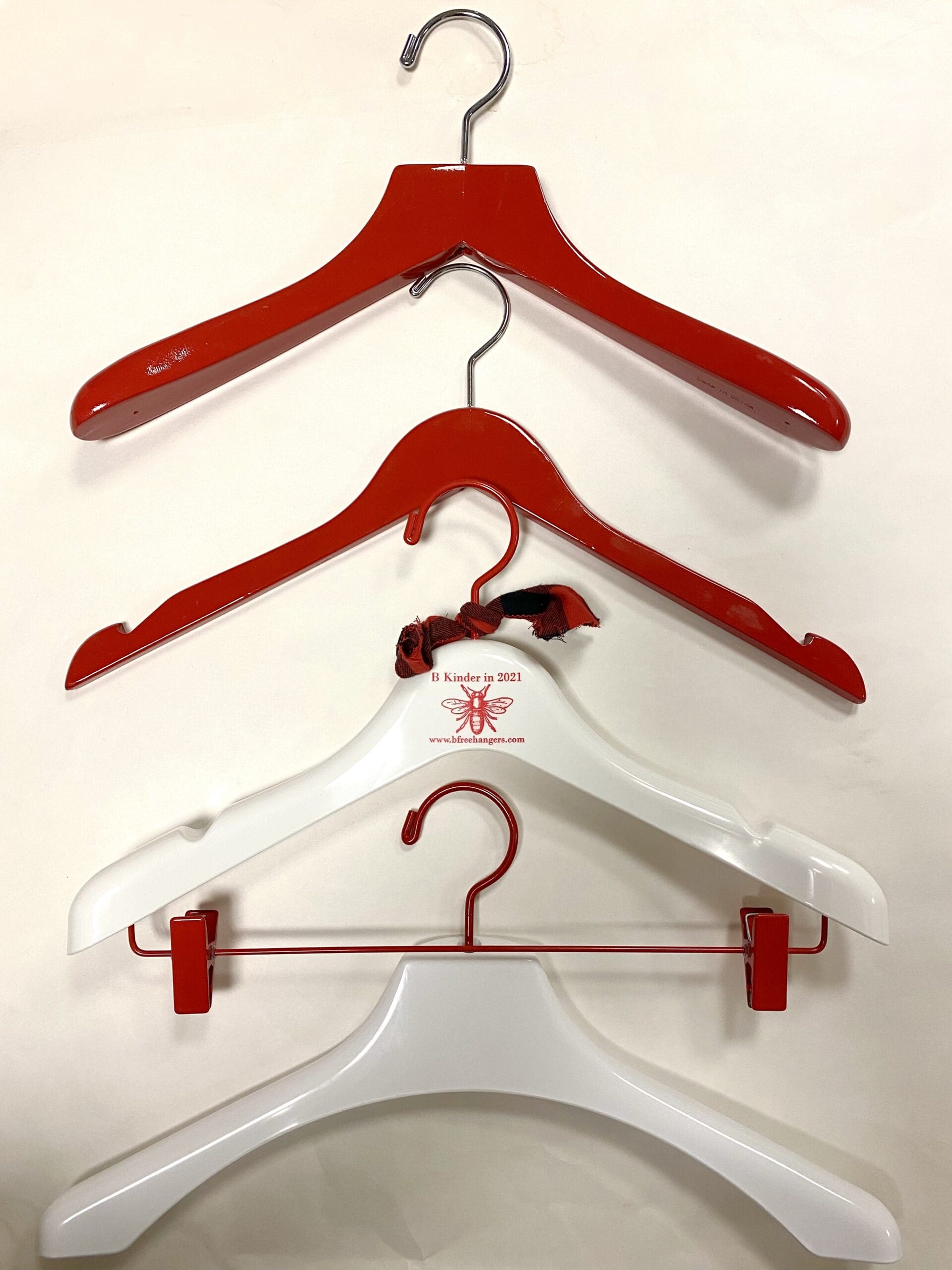 Four clothes hangers are displayed: two glossy red ones at the top and two white ones below, with one featuring a red clip, showcasing a variety of styles.
