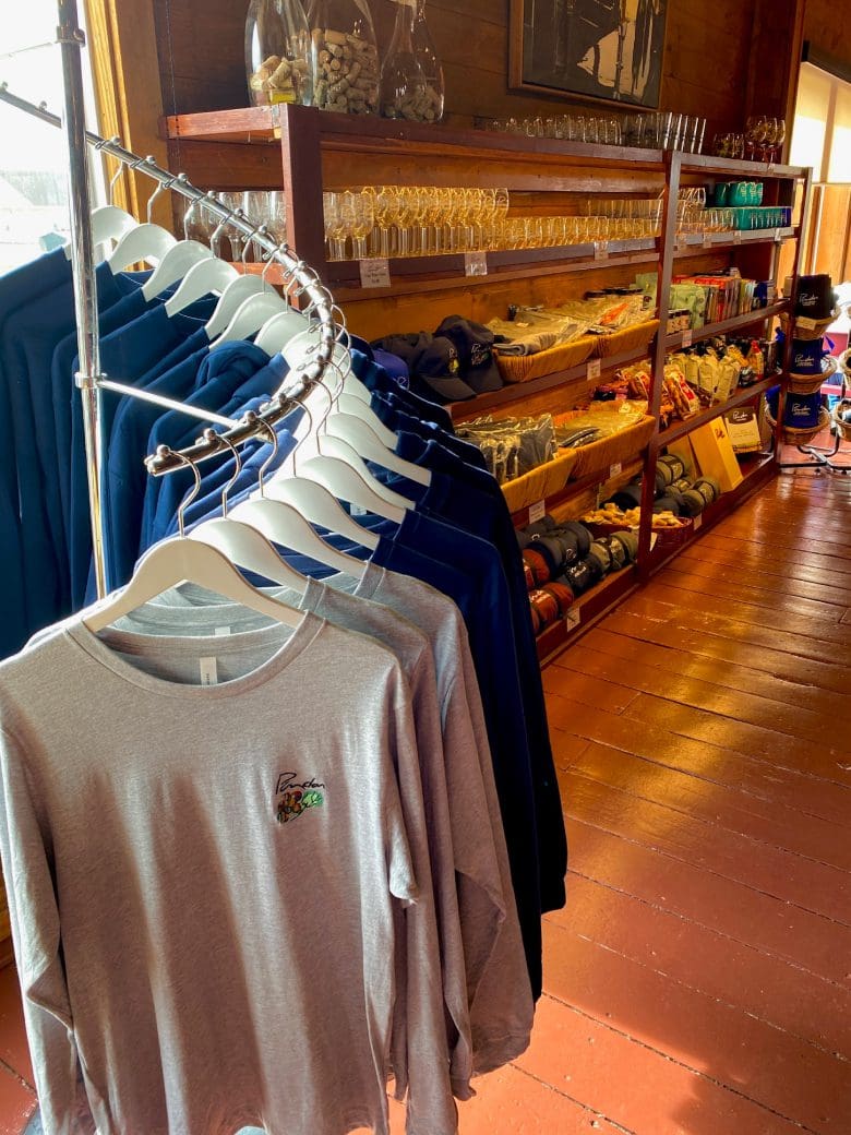 A retail space showcasing a rack of long-sleeve shirts and a display of various merchandise, including glassware and snacks, highlighting local products.