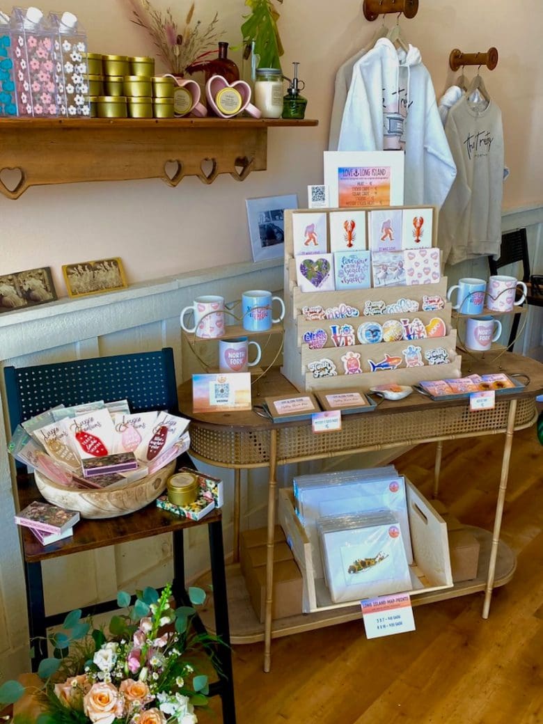 A vibrant display of local merchandise including mugs, stickers, and greeting cards, set in a cozy shop environment with floral arrangements.