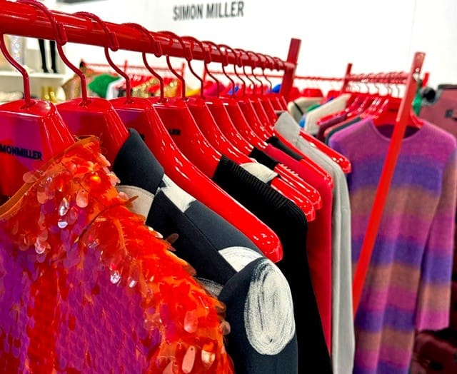 Simon Miller clothes hang on red hangers, varied styles.