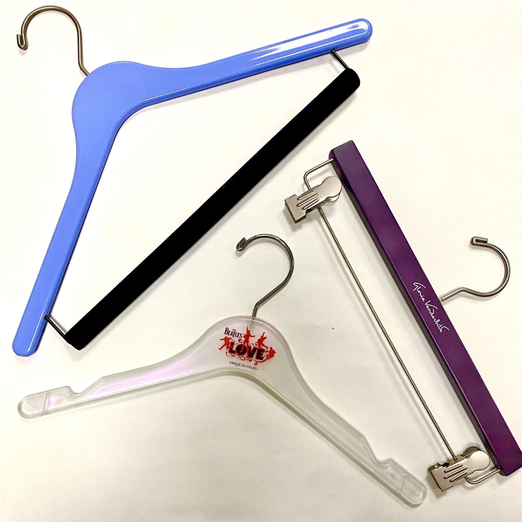 Various clothing hangers in different styles: a blue plastic hanger, a clear hanger with a Beatles “Love” logo, and a purple velvet hanger.