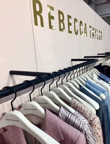 Display of Rebecca Taylor clothing on hangers, showcasing a variety of stylish garments against a branded backdrop.