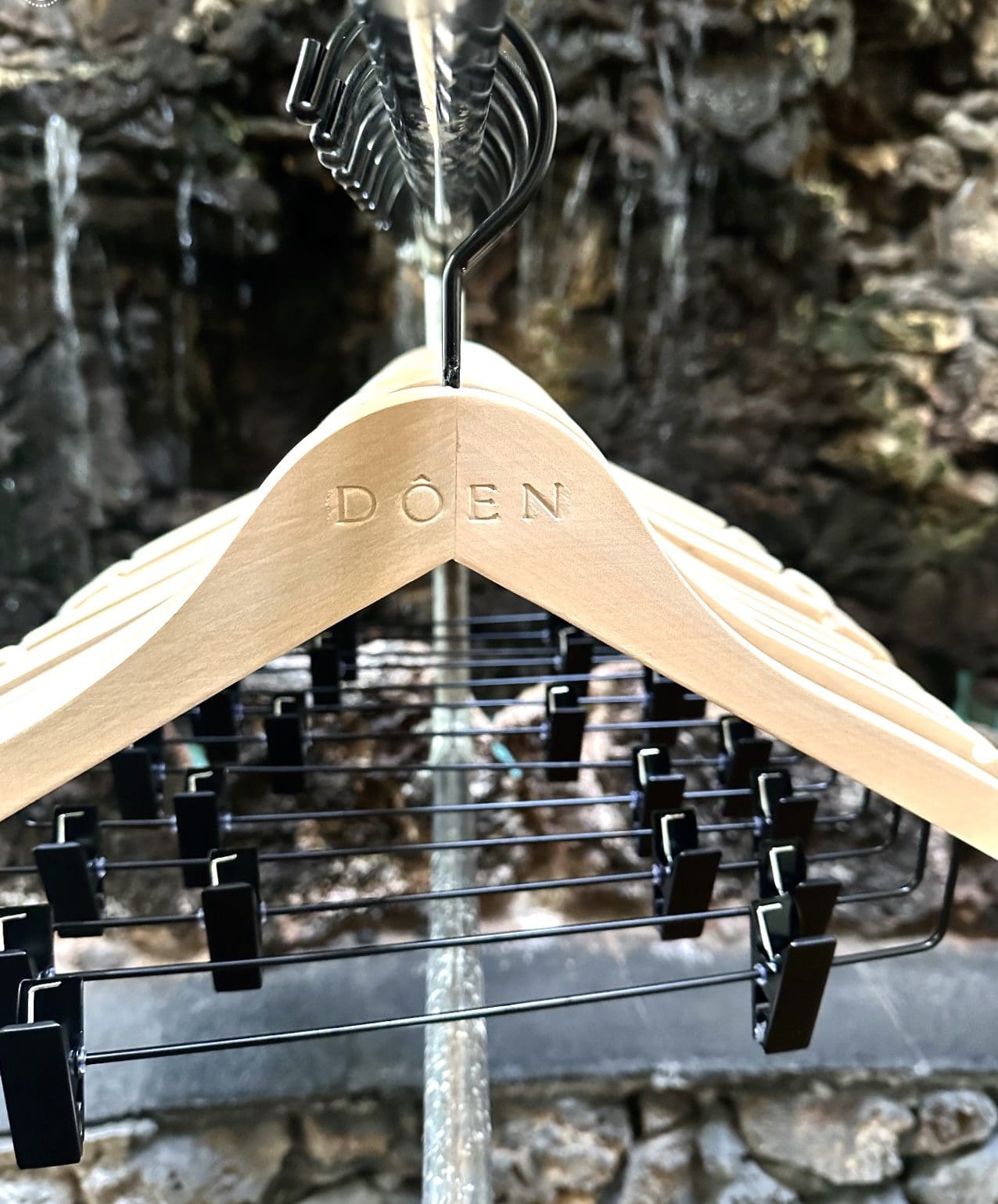 Close-up wooden hanger “DÔEN” with clips, stone background.