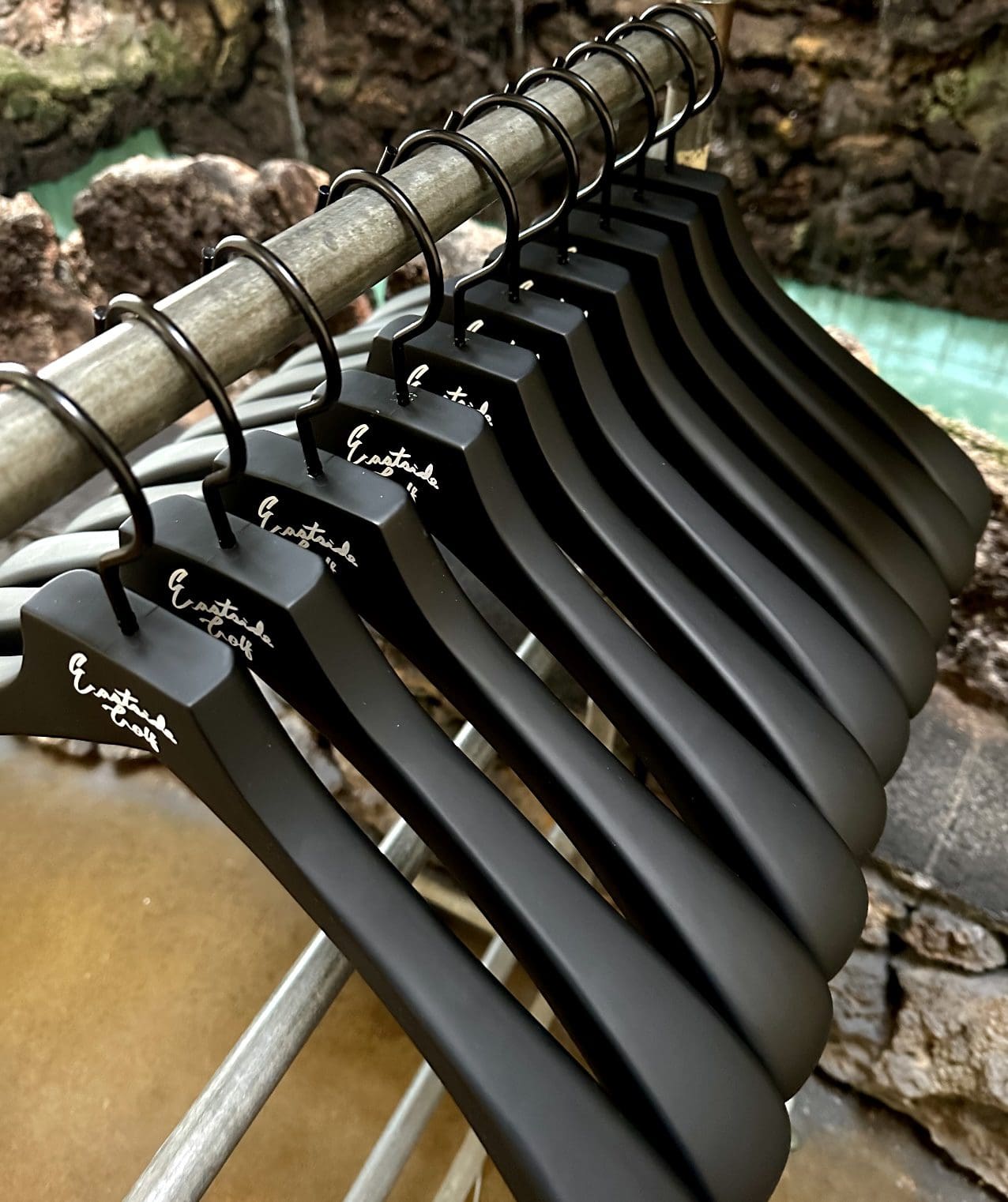 Row of black hangers with stylish logo on metal rack against textured background.