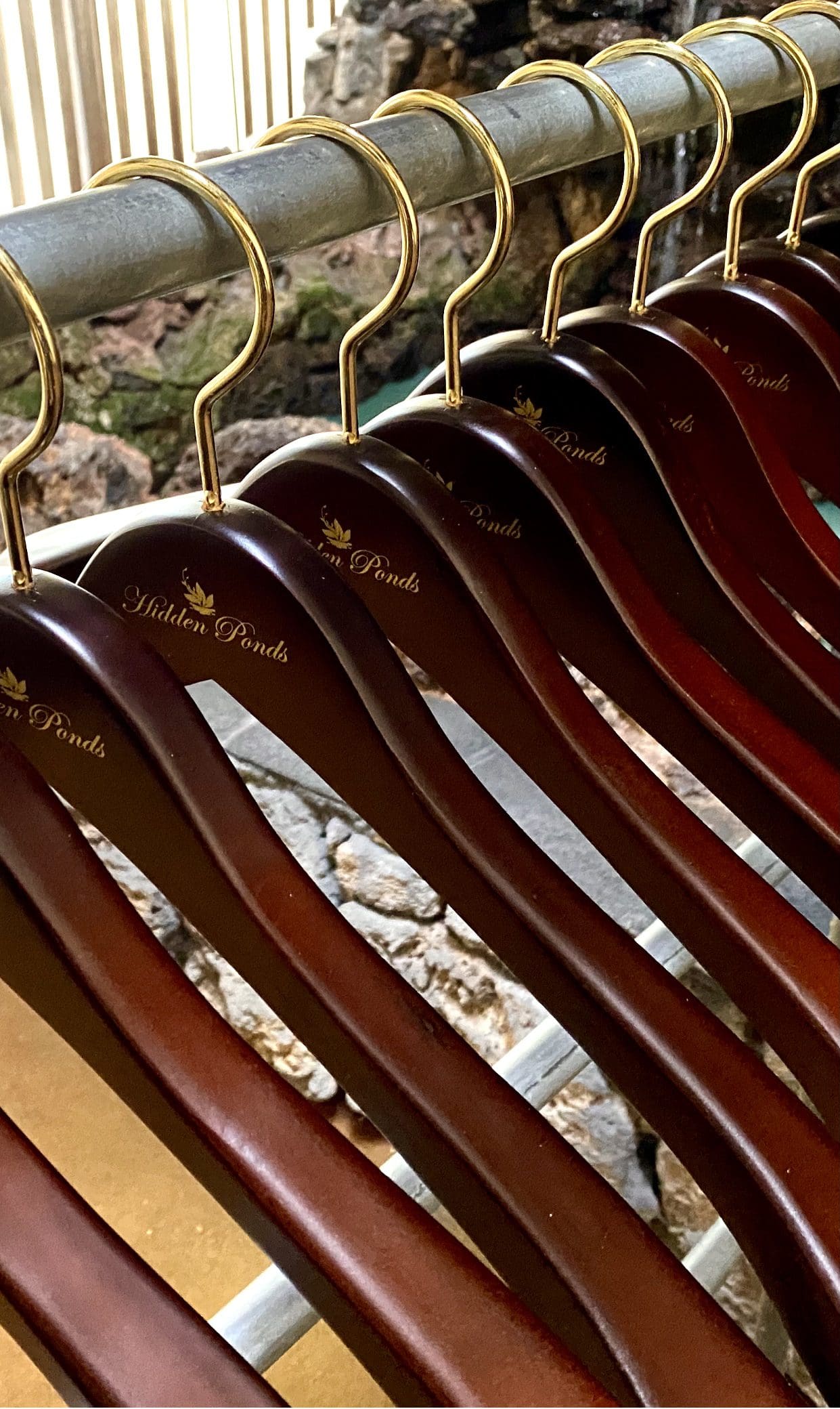 Row of elegant wooden hangers with gold hooks, labeled "Hidden Ponds," displayed in a serene setting, enhancing the aesthetic of a clothing presentation.