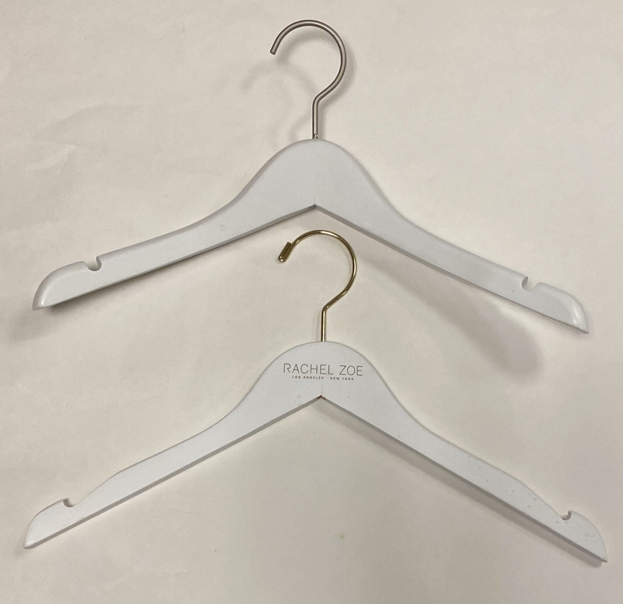 Two stylish white clothing hangers, one with a gold hook, both branded "Rachel Zoe," placed against a neutral background.