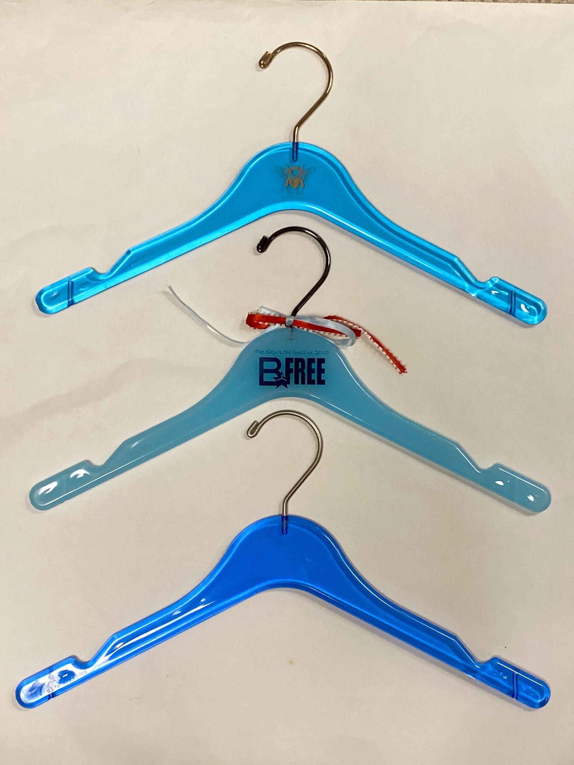 Three plastic hangers in varying shades of blue, displaying different hook designs. The bottom hanger has a "B FREE" label, showcasing organizational options.