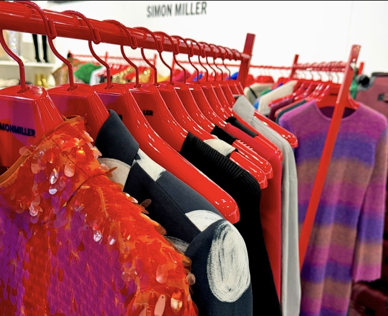 Colorful clothes on red hangers showcasing Simon Miller designs in store.