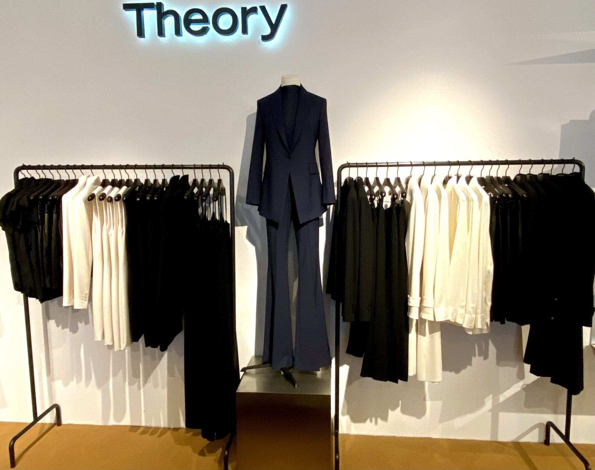 Navy Theory suit displayed amid modern black and white garments.