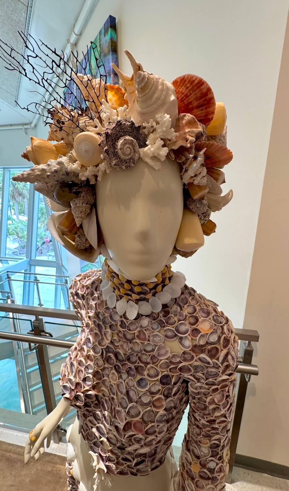 Mannequin wears vibrant seashell hat and shell-covered outfit.