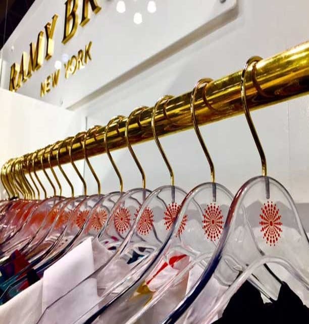 Clear acrylic floral hangers display clothing beneath fashion sign.