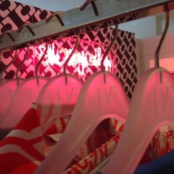 Colorful clothes hang on pink hangers, neon glowing.