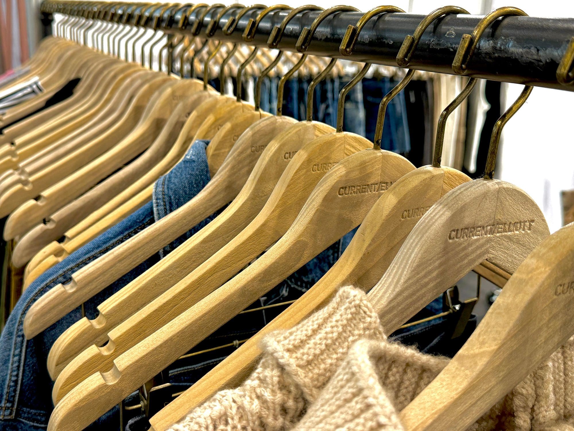 Wooden hangers showcase denim, knitwear in retail display.