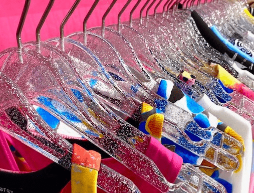 Colorful clothes on glittery hangers, pink backdrop.