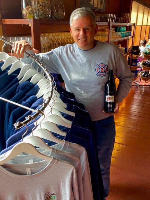 Man holding wine bottle beside sweatshirt rack in cozy shop.