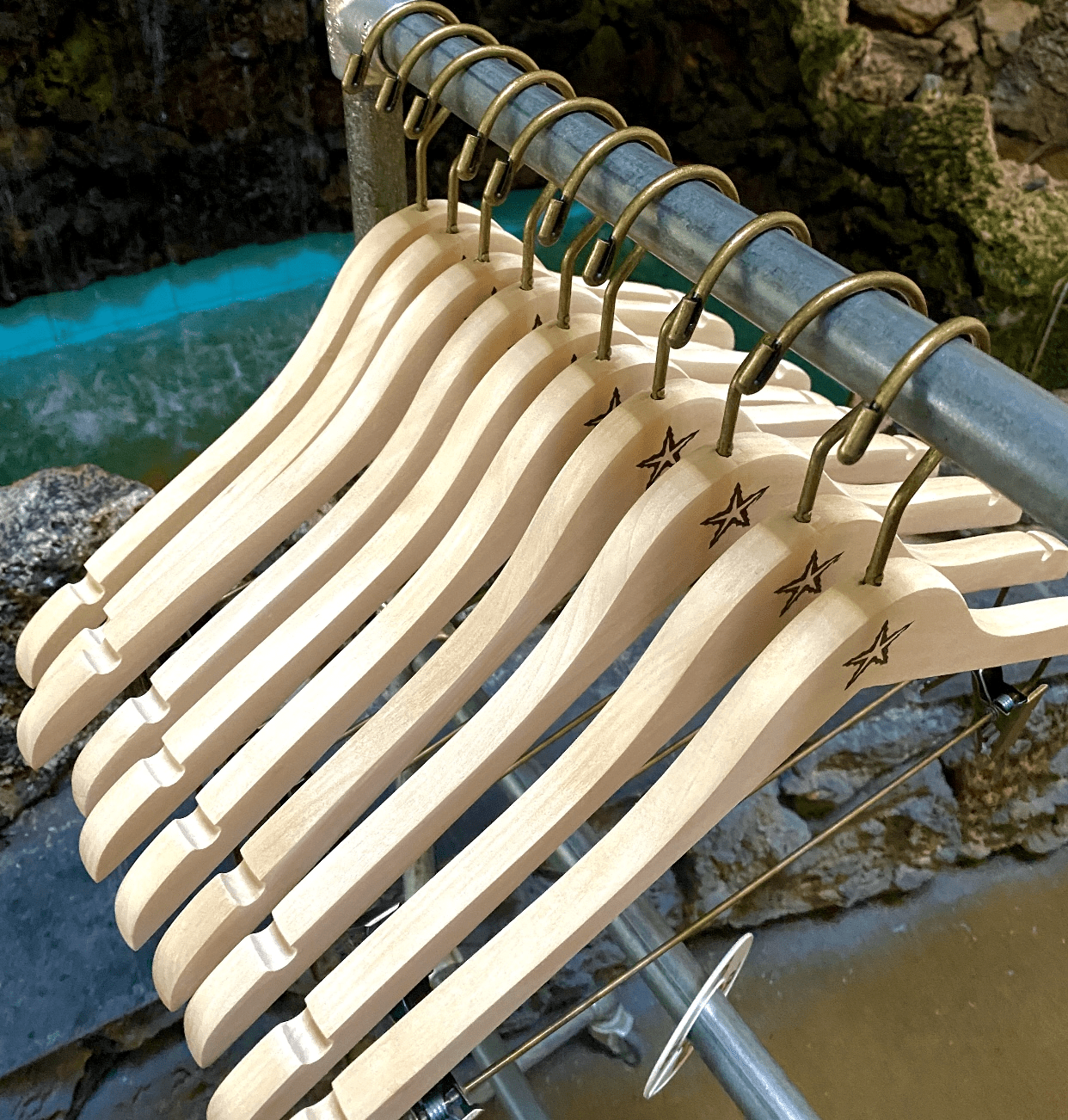 Wooden hangers are neatly arranged on a metal rack, with a soft blue waterfall in the background, suggesting a store display in a tranquil setting.