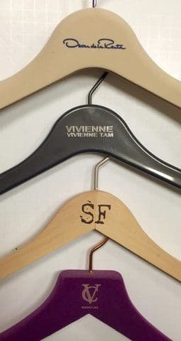 Fashion hangers showcase various brands, including Oscar de la Renta, Vivienne Tam, and a purple hanger labeled 'V.' Ideal for a fashion retail context.